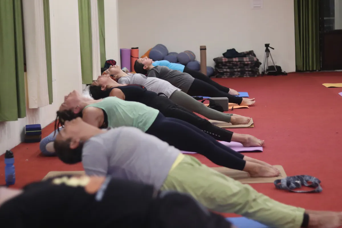 Yin yoga students resting in a reclining posture on mats in the yoga hall at Sri Yoga Ashram