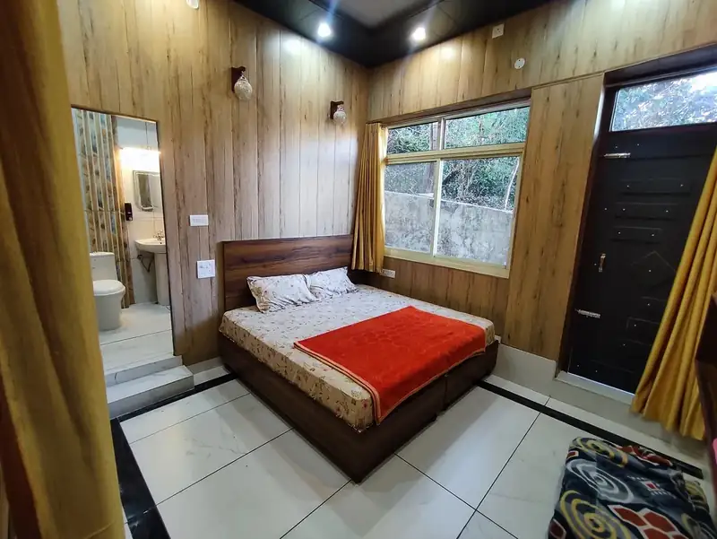Guest room at Sri Yoga Ashram Rishikesh with double bed, ensuite bathroom and window onto trees