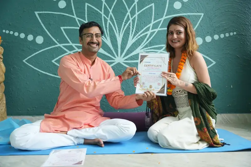 Teacher presenting yoga certificate to smiling student on mat at Sri Yoga Ashram Rishikesh