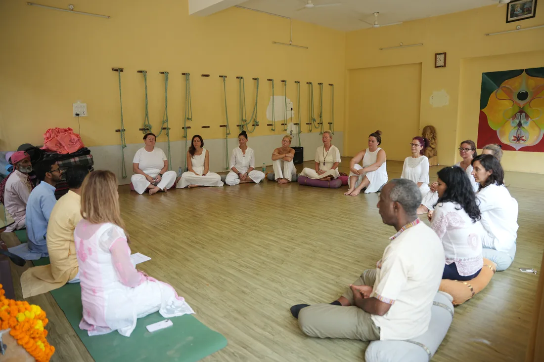 Teachers and students sitting in a wide satsang circle in the yoga hall, Rishikesh