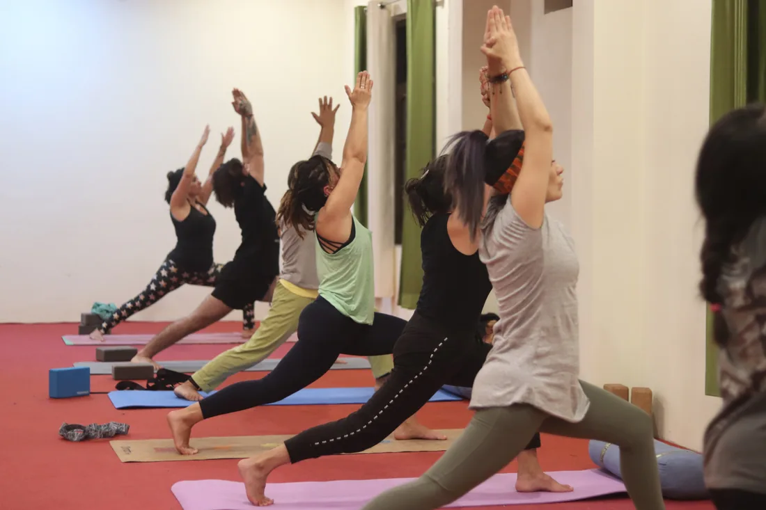 Students holding warrior one pose with arms raised in the Sri Yoga Ashram yoga hall